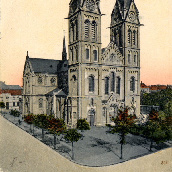 Eine Postkartenansicht der St.-Joseph-Kirche um 1910. Sie zeigt die beiden Kirchtürme mit ihren alten Kirchturmspitzen. Sie sind höher und spitzer als die Türme heute.