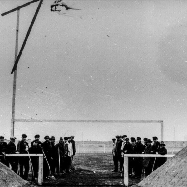 Eine Gruppe Arbeiter steht vor einem Fußballtor. Über ihnen hängt ein Richtkranz. Hinter ihnen liegt das fertiggestellte Spielfeld der Kampfbahn Glückauf.