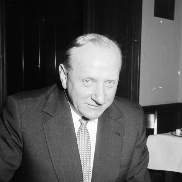 Fritz Szepan sitzt in einem Anzug und Krawatte an einem Tisch und füllt einen Wettschein aus. Unter dem Wettschein liegt eine aufgeschlagene Zeitung.