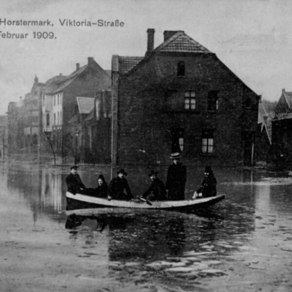 Ein kleines Boot mit sechs Personen an Bord fährt durch eine überflutete Stadt.