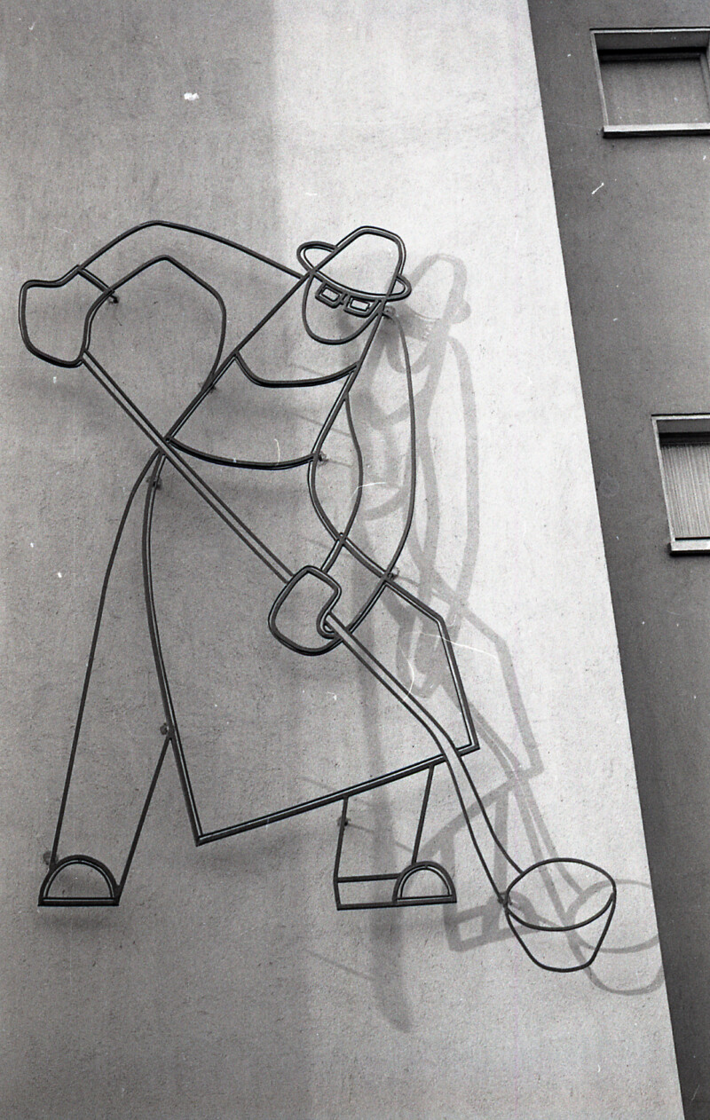 Auf einer Fassade sind die Umrisse eines Stahlarbeiters zu erkennen. Er trägt zum Schutz eine Schürze und Handschuhe. In den Händen hält er eine Gießkelle.