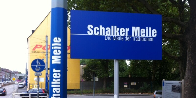 Auf einem blauen Schild steht in weißer Schrift "Schalker Meile - Die Meile der Tradition". Es ist an einer Straßenlaterne angebracht.