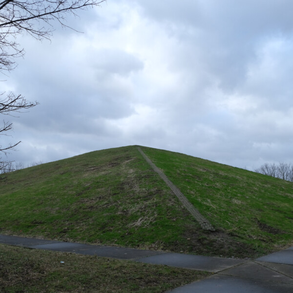 Eine kleine, mit Gras bewachsene Pyramide ragt in den bewölkten Himmel über Gelsenkirchen-Schalke.