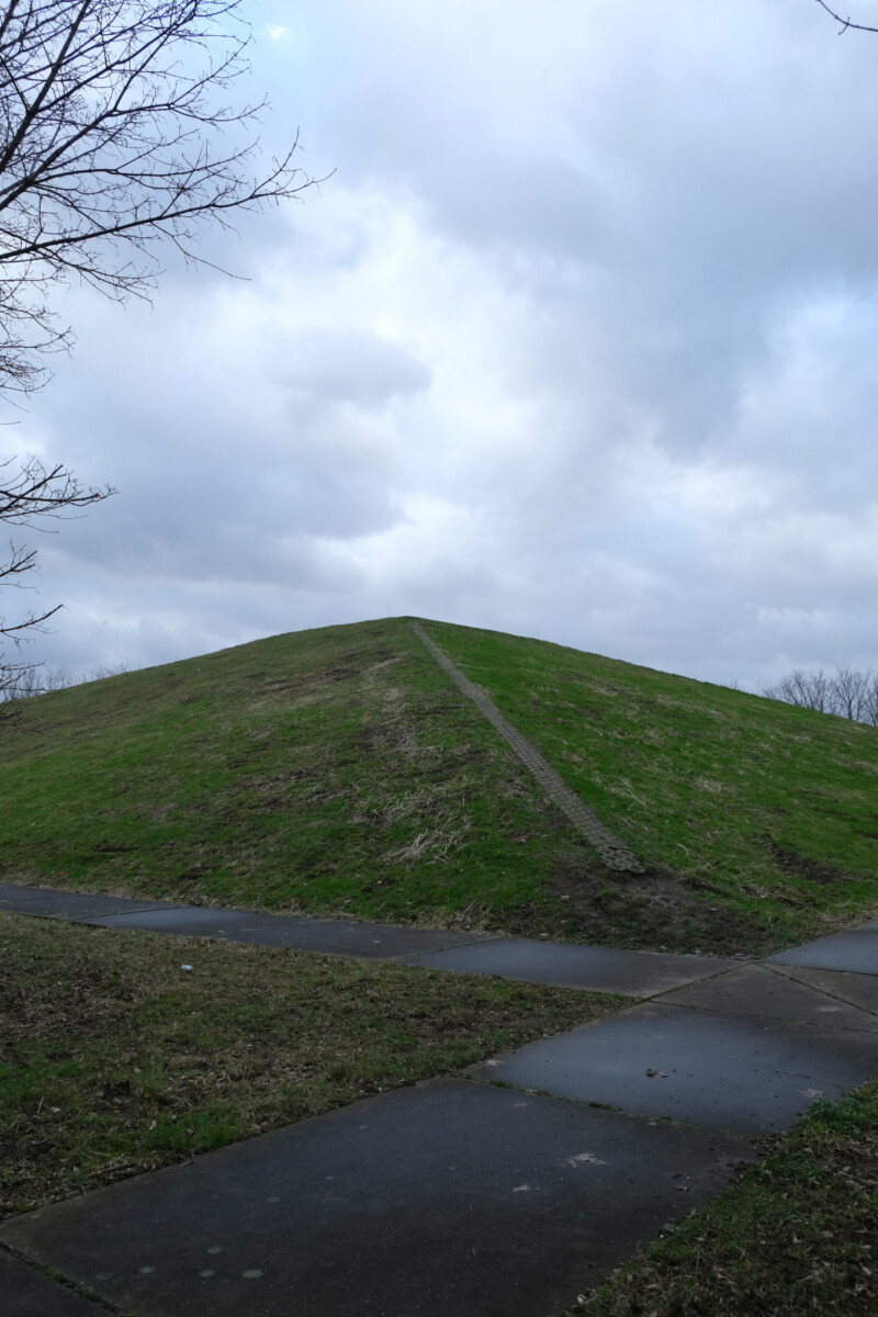 Eine kleine, mit Gras bewachsene Pyramide ragt in den bewölkten Himmel über Gelsenkirchen-Schalke.
