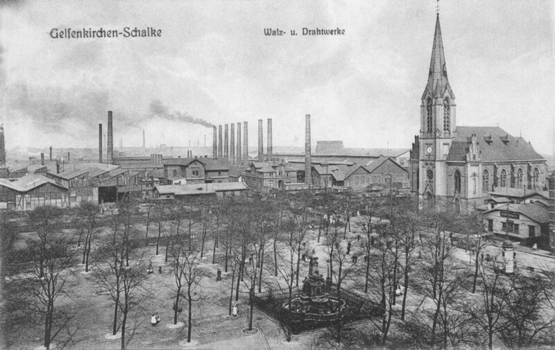 Eine Postkartenansicht in schwarz-weiß zeigt den Schalker Markt um das Jahr 1900. Der Schalker Markt ist mit Bäumen bewachsen. Zwischen ihnen steht der Grillo-Brunnen. Rechts steht die Evangelische Friedenskirche. Im Hintergrund ragen Schornsteine in den Himmel.