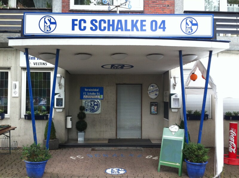 Heute ist der Eingang zum Vereinslokal "Bosch" an der Kampfbahn Glückauf in Schalke überdacht. Auf dem Dach ist über die ganze Breite angebracht. Auf dem Schild steht "FC Schalke 04".