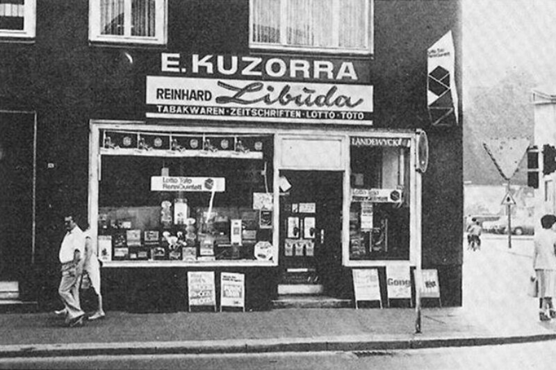 Frontansicht des Tabakladens. Über dem Eingang hängt ein Schild mit der Aufschrift "E. Kuzorra, Reinhard Libuda".