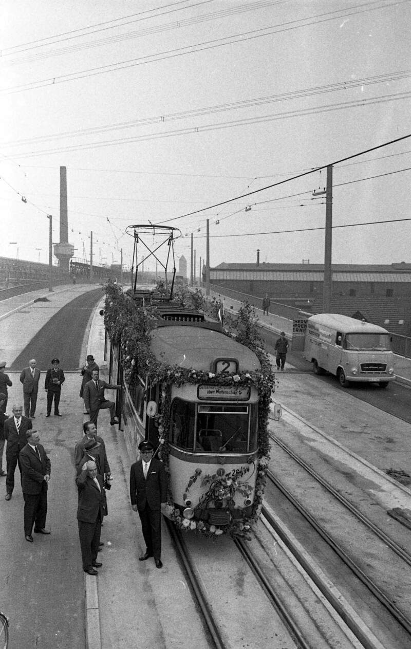 Eine blumengeschmückte Straßenbahn der Linie 2 steht auf der fertiggestellten Hochbrücke Berliner Brücke. Um sie herum stehen Männer in Anzügen und zwei Angestellte der Bahngesellschaft. Sie sind an ihrer Dienstuniform und Dienstmütze zu erkennen.