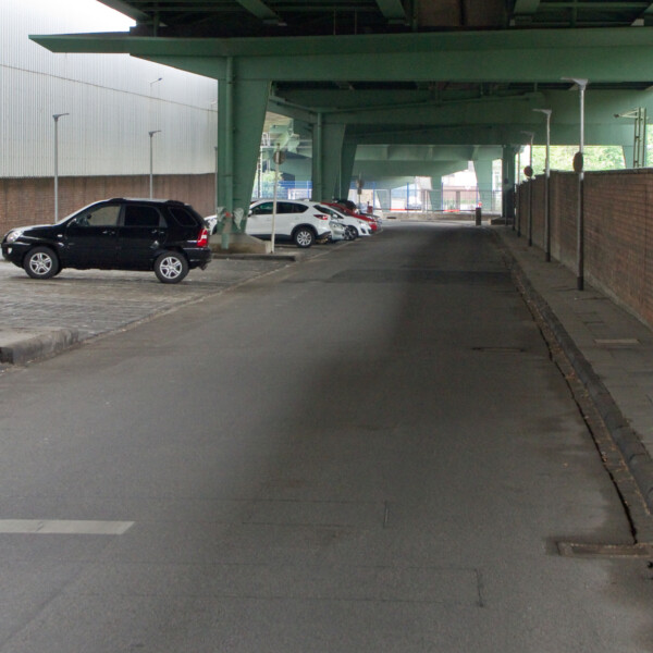 Ansicht der Straße unter der Berliner Brücke am Schalker Markt. Erkennbar sind die grünen Stahlträger der Brücke. Unter ihr liegt eine verlassene Straße. An der Seite parken vereinzelt Autos.