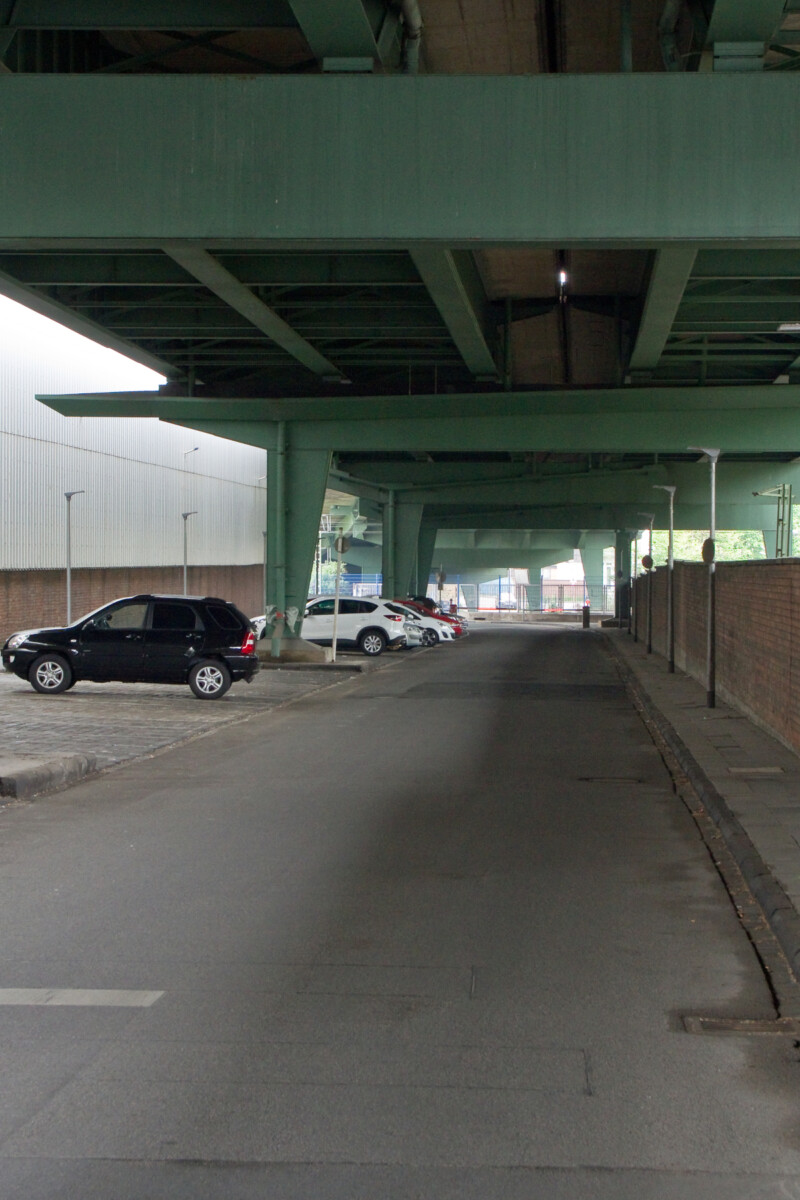 Ansicht der Straße unter der Berliner Brücke am Schalker Markt. Erkennbar sind die grünen Stahlträger der Brücke. Unter ihr liegt eine verlassene Straße. An der Seite parken vereinzelt Autos.