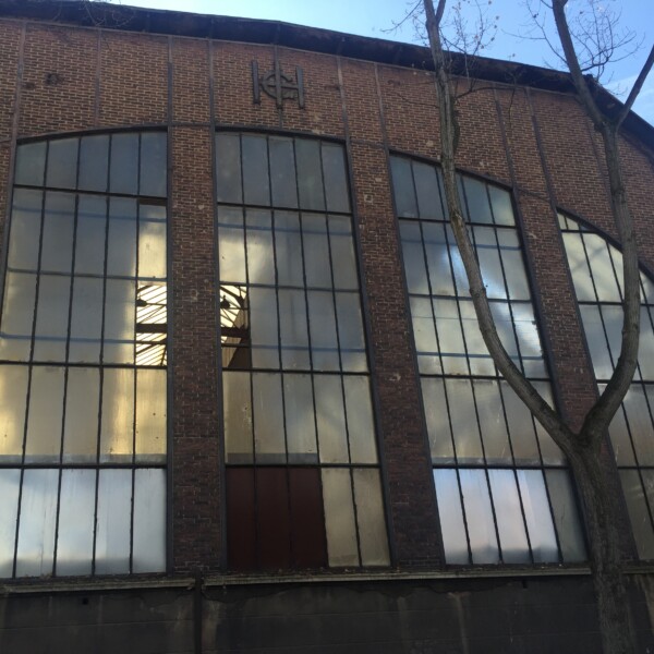 Nahaufnahme der Front der Gutehoffnungshütte. Ein Fensterbogen nimmt den Großteil des Bildes ein. Darüber hängen die Buchstaben G, H und H als Emblem der Gutehoffnungshütte.