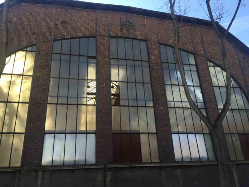 Nahaufnahme der Front der Gutehoffnungshütte. Ein Fensterbogen nimmt den Großteil des Bildes ein. Darüber hängen die Buchstaben G, H und H als Emblem der Gutehoffnungshütte.