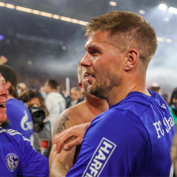 Simon Terodde steht verschwitzt im Schalke-Trikot in einer Menge jubelnder Menschen auf dem Spielfeld der Arena.