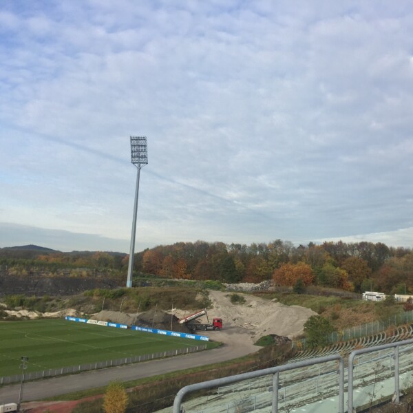 Blick von den Resten der überwucherten Tribüne des Parkstadions. Im Hintergrund schüttet ein LKW Material auf.