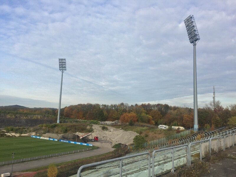 Blick von den Resten der überwucherten Tribüne des Parkstadions. Im Hintergrund schüttet ein LKW Material auf.