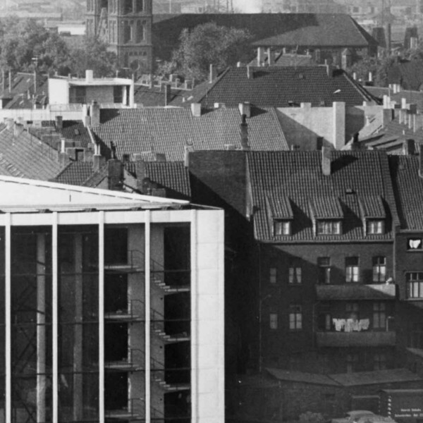 Detailansicht der rechten Ecke der Glasfassade des Musiktheaters im Revier. Im Hintergrund stehen die St.-Joseph-Kirche und Teile der Schalker Industrie.