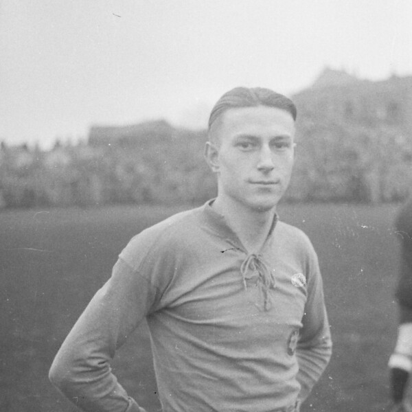 Hermann Eppenhoff steht als junger Spieler auf dem Feld eines Stadions. Die Zuschauerränge im Hintergrund sind voller Menschen.