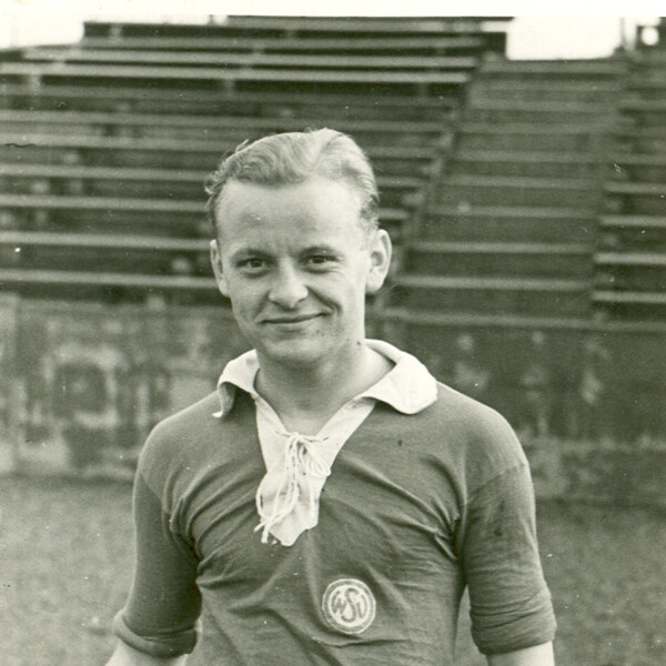 Der junge steht als junger Spieler in einem Trikot des Westdeutschen Spielverbandes (WSV) vor einer leeren Tribüne und lächelt in die Kamera.