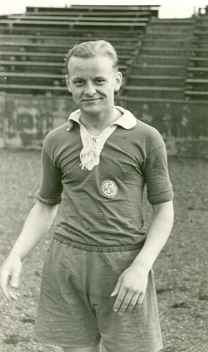 Der junge steht als junger Spieler in einem Trikot des Westdeutschen Spielverbandes (WSV) vor einer leeren Tribüne und lächelt in die Kamera.